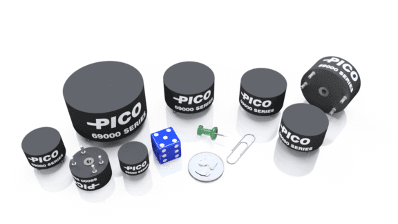 Several Pico 69000 Series cylindrical components are arranged alongside a blue die, a green thumbtack, a paperclip, and a coin for scale, on a white surface.