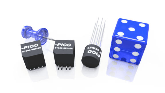 Electronic components labeled "PICO 81000 SERIES" and "PICO 71000 SERIES," a pushpin, and a blue six-sided die are arranged on a shiny surface.